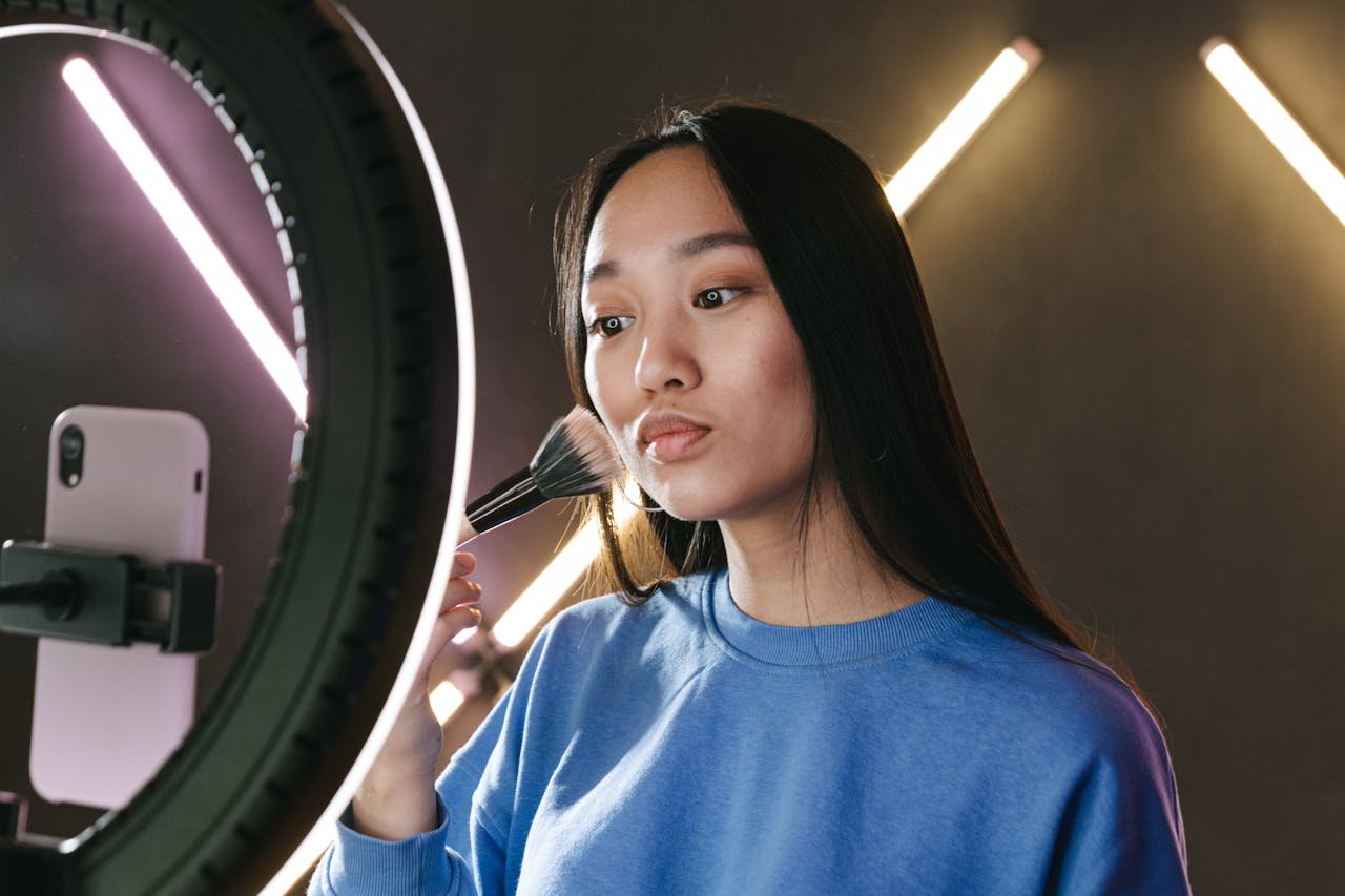 why-choose-us Asian woman filming a makeup tutorial for her vlog using a ring light, emphasizing beauty and creativity.